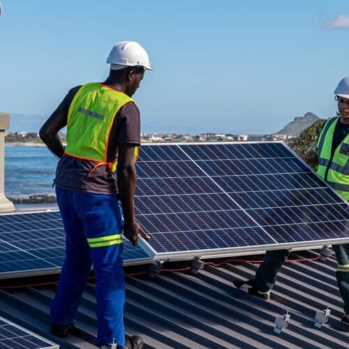 two workers install solar panels on roof